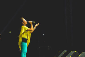 Female singing on stage wearing yellow top and green pants