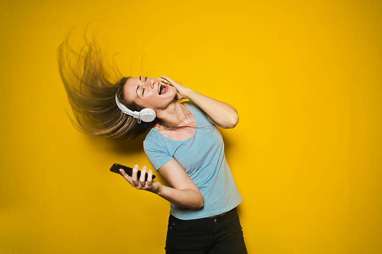 Female singing loudly wearing headphones against yellow background